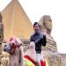Un touriste chinois se fait photographier à dos de chameau devant une pyramide égyptienne dans un parc d